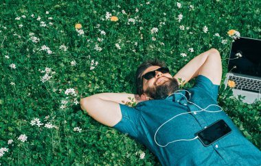 Onun dizüstü bilgisayarın yakınında çim üzerinde yalan yorgun serbest meslek. Ellerini başının arkasında ile dinlenme güneş gözlüğü yakışıklı adam