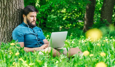 Bilgisayarda çalışarak ve çim üzerinde oturan genç modern işadamı serbest meslek. Erkek öğrenci Not defteri açık havada kullanarak. Dizüstü bilgisayarda çalışan Turizm