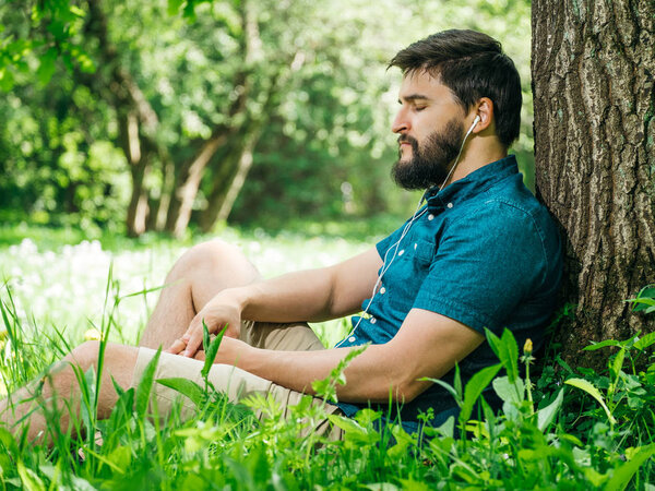 Молодой человек слушает музыку в зеленом летнем лесу и расслабляется
