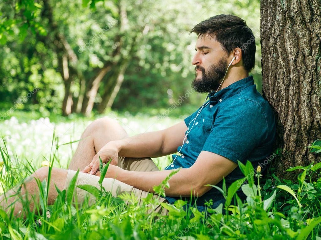 Молодой человек слушает музыку в зеленом летнем лесу и расслабляется