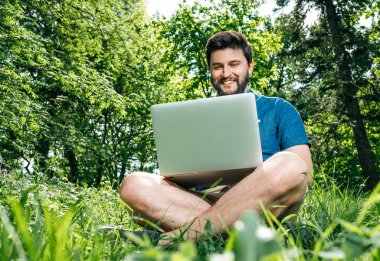 Bilgisayarda çalışarak ve çim üzerinde oturan genç modern işadamı serbest meslek. Erkek öğrenci Not defteri açık havada kullanarak. Dizüstü bilgisayarda çalışan Turizm