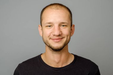 Gülümseyen genç adam portresi. Kameraya bakarak gri arka plan üzerinde yakışıklı genç