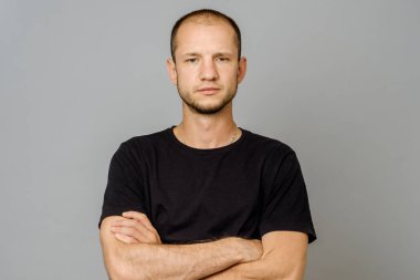Siyah t-shirt gri arka plan üzerinde çapraz kolları olan ciddi genç adam