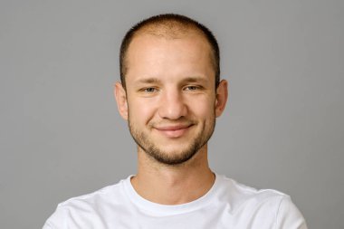 Gülümseyen genç adam portresi. Kameraya bakarak gri arka plan üzerinde yakışıklı genç