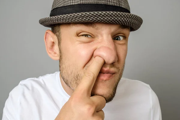 男子采摘他的鼻子 男人的情感肖像在帽子和空白 T恤衫 灰色背景 — 图库照片