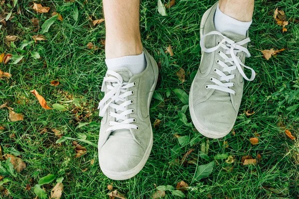 Male feet in gray gumshoes on green grass