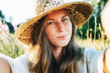 Güzel sarışın genç gülümseyen Park doğa arka plan üzerinde hasır şapkalı kadın kendi portresi. Seyahat. Selfie