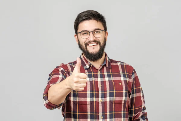 El joven sostiene su pulgar hacia arriba. Aislado en gris — Foto de Stock