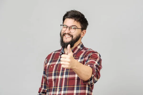 El joven sostiene su pulgar hacia arriba. Aislado en gris — Foto de Stock