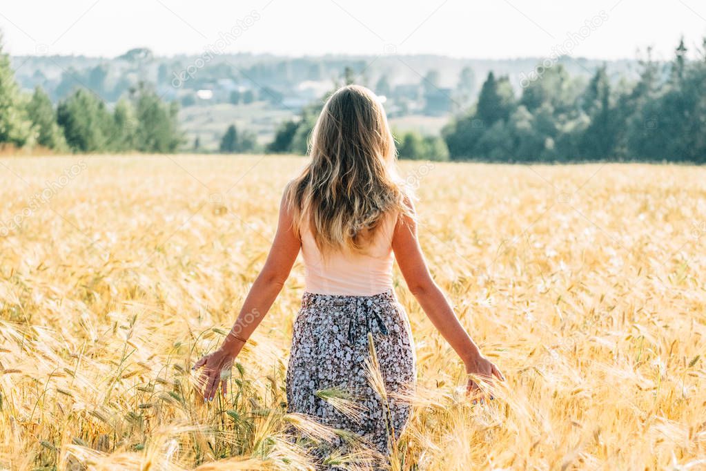 Young woman in dress walking along cereal field