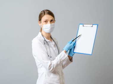 Koruyucu maske takan kadın doktor beyaz kağıtlı panoyu gösteriyor. Gri renkte izole edilmiş