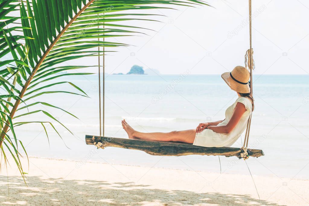 Young woman sitting on a beach swing. Happy female traveller. Vacation concept