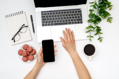 Kadın el ele tutuşmasını ve bilgisayarın arka planında boş ekranlı siyah cep telefonu kullanmasını görüntüle. Üst Manzara. Düz yatıyordu
