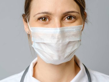 Krizi çözmek için ameliyat maskesi takan mutlu bir doktor. Gri arkaplanda izole