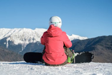 Spor giyimli snowboardcuların arka görüntüsü. Ekipmanlar kayak pistinin tepesinde dinleniyor ve manzaranın keyfini çıkarıyorlar.