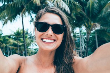 Tropiklerde gülümseyen mutlu bayan turistin yakın plan çekimi plajda okyanus kenarında boş zamanın tadını çıkarıyor. Yaz günü boş zamanlarında kameraya bakar. Selfie pozları