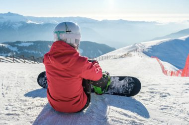 Spor giyimli snowboardcuların arka görüntüsü. Ekipmanlar kayak pistinin tepesinde dinleniyor ve manzaranın keyfini çıkarıyorlar.