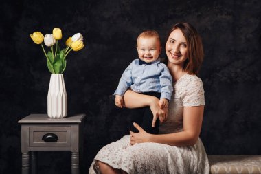 Grup birlikte kanepede kapalı oturan beyaz güzel beyaz kadın anne-baba ve oğlu bebek çocuk portresi. Mutlu anne gün tatil kavramı. Kadın çocuk çocuğunu sarılma