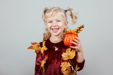 Çok güzel komik beyaz sarışın beyaz kız portre sarı sonbahar yaprakları ile Cadılar Bayramı için giyinmiş. Eğleniyor studio sonbahar mevsim tatil için oynayan çocuk. Küçük oyuncak kabak tutan çocuk