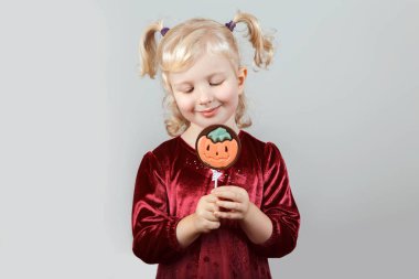 Çok güzel komik beyaz sarışın beyaz kızla pigtails portresi Cadılar Bayramı için giyinmiş. Eğleniyor studio sonbahar sonbahar mevsim tatil için oynayan çocuk. Çocuk yeme çikolata lolipop