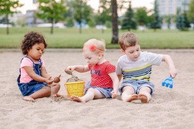 Plastik renkli oyuncaklar ile oynama sandbox oturan üç sevimli beyaz ve İspanyol latin küçük çocuklar bebekler çocuk portresi. Küçük kız ve erkek arkadaş sahada birlikte eğleniyor. 