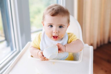 Sevimli sevimli beyaz çocuk çocuk sandalyesi yeme elma püresi ile parmak oturan kirli pis yüzü ile portresi. Her gün eve çocukluk bir yaşam tarzı. Bebek çalışırken takıma giren bebek maması