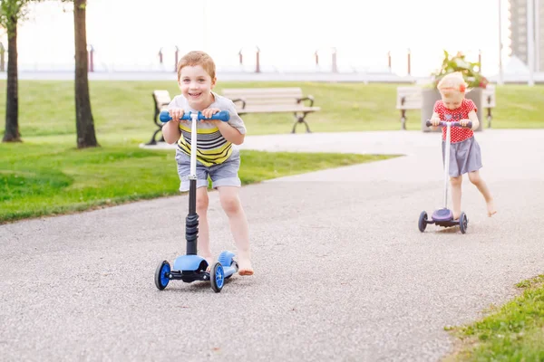两个活跃的小朋友的肖像在夏天的户外公园里 女孩和男孩骑着滑板车上路 季节性儿童活动运动 健康的童年生活 — 图库照片
