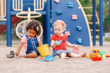 Baktılar bak. İki sevimli beyaz ve İspanyol latin plastik renkli oyuncaklar ile oynama sandbox oturan çocuk bebekler. Küçük kız arkadaş sahada birlikte eğleniyor.