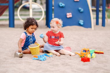 Masum bak. İki sevimli beyaz ve İspanyol latin plastik renkli oyuncaklar ile oynama sandbox oturan çocuk bebekler. Küçük kız arkadaş sahada birlikte eğleniyor.