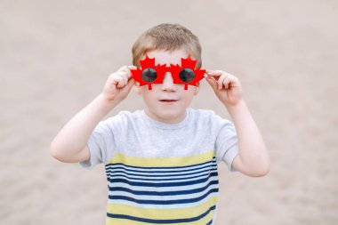 Akçaağaç yaprağı ile komik Kanada güneş gözlüğü takıyor sevimli sevimli küçük sarışın beyaz çocuk portresi. Kanada günü kutluyor ve having fun çocuk çocuk. 