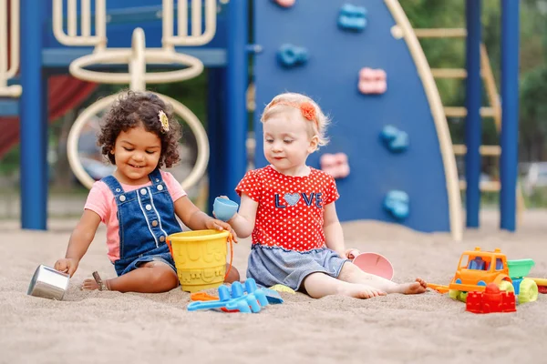 Yaz ruh. İki sevimli beyaz ve İspanyol latin plastik renkli oyuncaklar ile oynama sandbox oturan çocuk bebekler. Küçük kız arkadaş sahada birlikte eğleniyor.