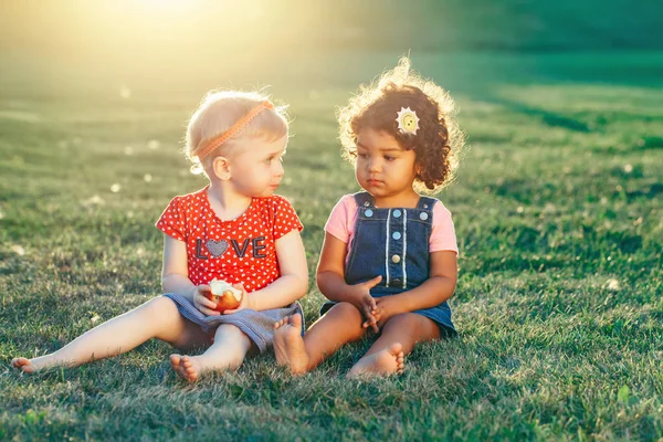 共有のリンゴを一緒に座っている白人およびラテン系の白人のヒスパニック女の子子供のグループの肖像画 つの夏の日の公園で外食べるフルーツを赤します 親友は永遠に 児童の健全です — ストック写真