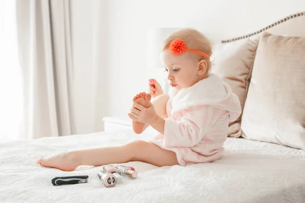 可爱的金发白人女孩画指甲坐在家里的床上 女孩子做指甲和吹干 幼儿玩使用化妆品 — 图库照片