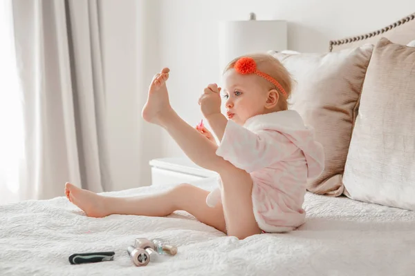 可爱的金发白人女孩画指甲坐在家里的床上 女孩子做指甲和吹干 幼儿玩使用化妆品 — 图库照片