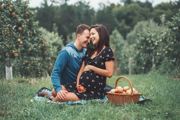 Happy healthy pregnancy and parenting. Portrait of pregnant young brunette Caucasian woman with husband on apple farm. Beautiful expecting mother and future father at countryside, rustic style