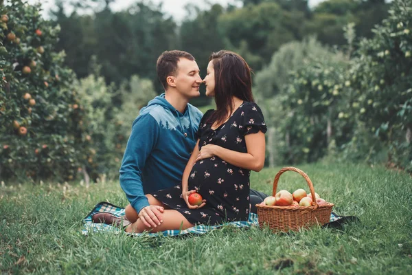 Happy healthy pregnancy and parenting. Portrait of pregnant young brunette Caucasian woman with husband on apple farm. Beautiful expecting mother and future father at countryside, rustic style