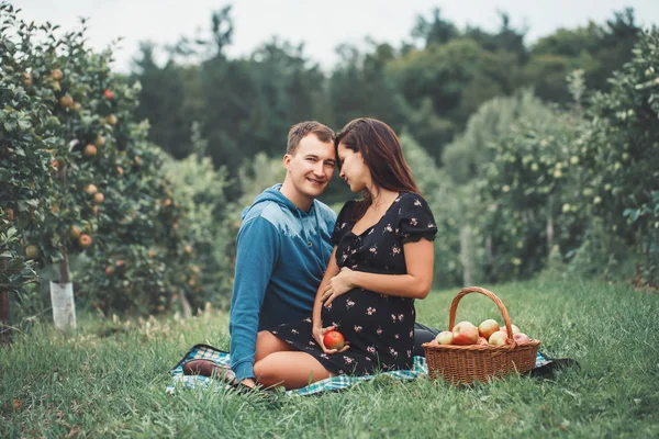 Happy healthy pregnancy and parenting. Portrait of pregnant young brunette Caucasian woman with husband on apple farm. Beautiful expecting mother and future father at countryside, rustic style