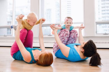 Grup iki genç kadını çocuklu beden eğitimi dersinde gevşek bebek kilo için egzersiz yapıyor. Çocuklara annelerin çocukları ile uygunluk. Anneler için Aile aktivitesi kavramı yaşam tarzı.