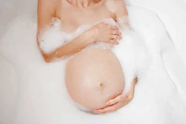 Beyaz beyaz hamile kadın alarak banyo köpüğü, closeup üstten Yukarıdaki görüntüleyin. Bekliyor kadın Bayan Anne karnı dokunmadan tutarak. Genel gider görüntü alışılmadık açı.
