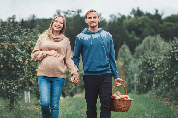 Happy healthy pregnancy and parenting. Portrait of pregnant young blonde Caucasian woman with husband on apple farm. Beautiful expecting mother and future father at countryside, rustic style
