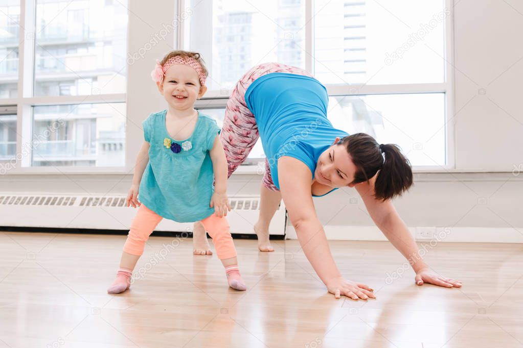Young woman with child daughter doing workout in gym class to loose baby weight. Child-friendly fitness for mothers with kids toddlers. Lifestyle concept of family activity indoors.