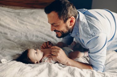 Yeni doğan bebek oğlu kızı konuşuyor orta yaş beyaz baba portresi. Çocuk yatak odası evde yatakta üzerinde gülümseyen erkek üst. Otantik yaşam tarzı çok samimi an. 