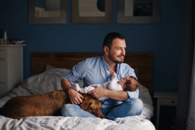Orta yaş beyaz baba ile yeni doğan bebek portresi. Köpek evde beslenen hayvan yatak üzerinde döşeme. Adam üst elinde tutma. Otantik yaşam tarzı documenatry an. Bekar Baba aile hayatı. 