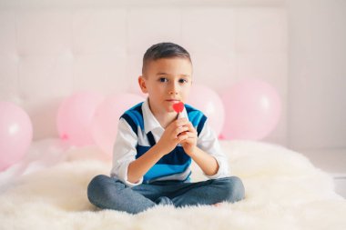 Sevgililer günü tatil kutluyor kalp şeklinde lolipop yemek beyaz beyaz sevimli sevimli çocuk çocuk portresi. Yatak yatak odasında oturup şeker çocuk. 