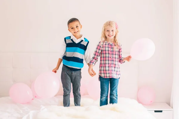 两个快乐的白人白种人可爱可爱有趣的孩子站在卧室的床上的合影 男孩和女孩有乐趣与粉红色的气球 友谊和乐趣 永远最好的朋友 — 图库照片