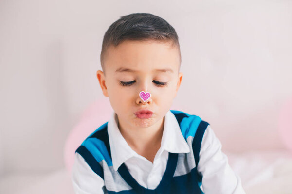 Funny hilarious authentic white Caucasian cute adorable child boy looking at her nose with heart sticker on it. Valentine day holiday concept.