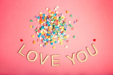 Mutlu sevgililer günü. Pembe mercan arka plan üzerinde renkli kalpler şeker yığını ile güzel kart. Şubat tatil kavramı. Ahşap kelime harf söyleyerek seni seviyorum. 