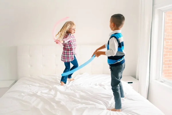 Two Caucasian cute adorable funny children jumping on bed in bedroom and playing. Boy and girl are having fun fighting with balloons. Best friends forever. Happy childhood lifestyle. Motion blur