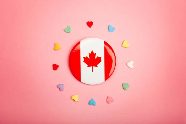 Happy Canada Day greeting card with Canadian flag in centre middle and many colorful candies hearts around it on living coral pink background. Multiculturalism national values concept.