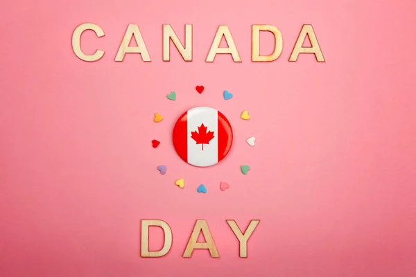 Happy Canada Day greeting card with wooden letters. Words and Canadian flag with many candies hearts around it on living coral pink background. Multiculturalism national values concept.